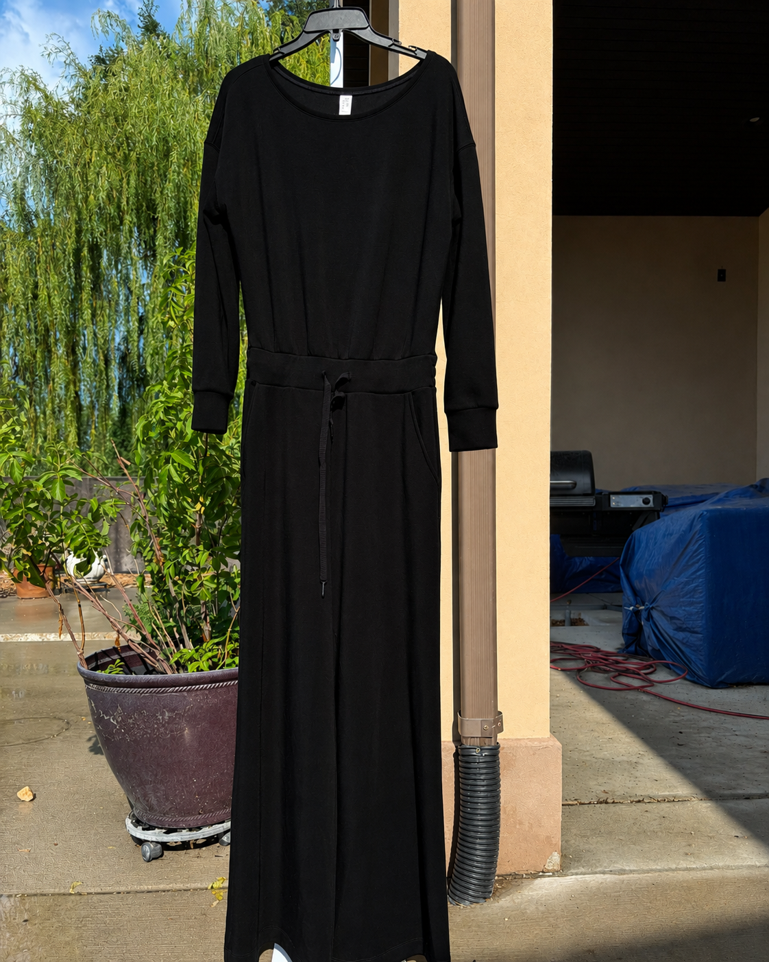 SPANX AirEssentials deep black jumpsuit with a wide boat neckline, relaxed long sleeves, pockets, and full-length wide legs.